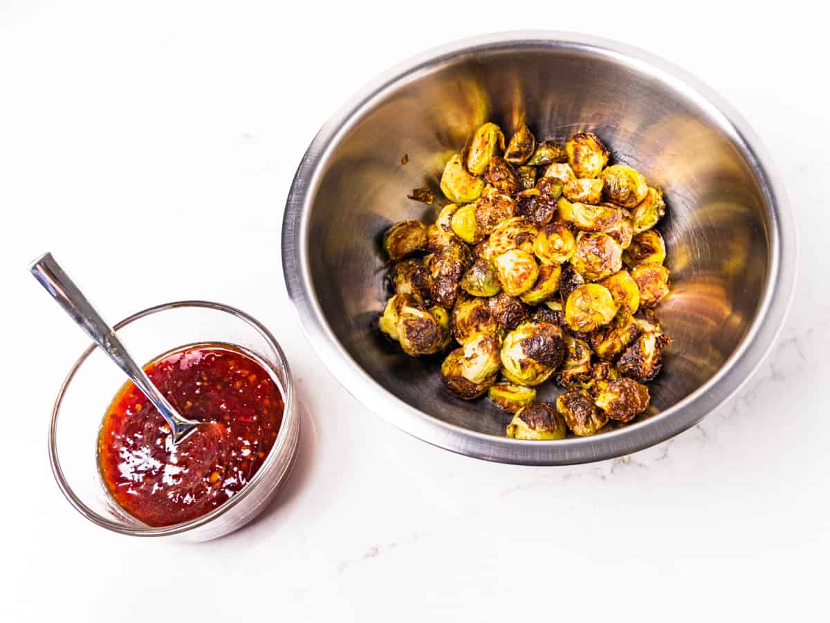 Roasted Brussels sprouts in a bowl alongside a bowl of Thai chili sauce.