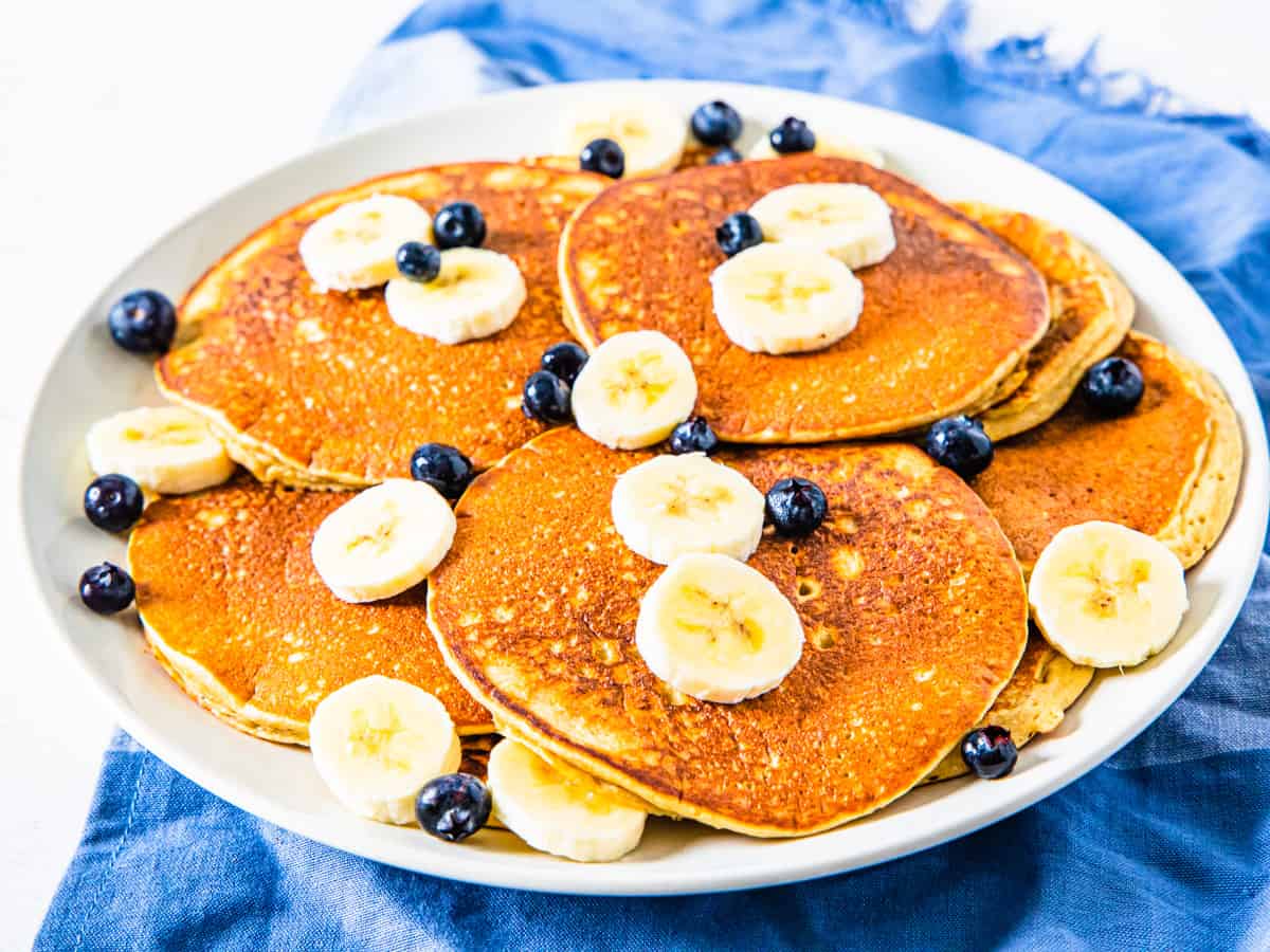 A plate of pancakes topped with blueberries and sliced bananas.