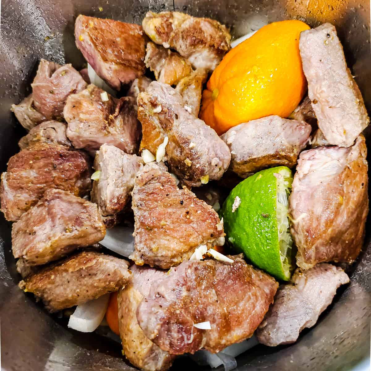 Seared pork chunks with citrus and mojo sauce in an Instant Pot before pressure cooking.