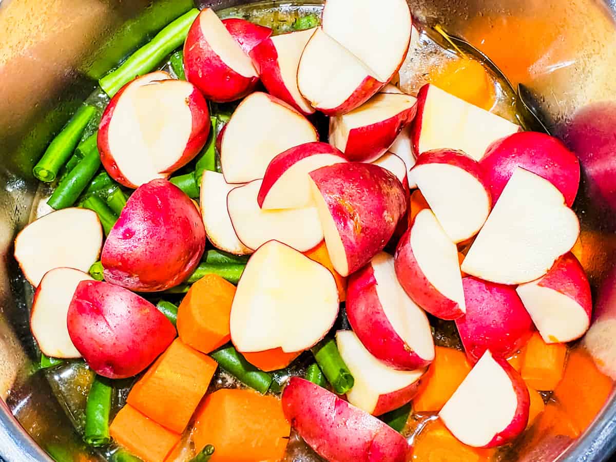 Potatoes, carrots, and green beans shown in an Instant Pot, before cooking with the stew.