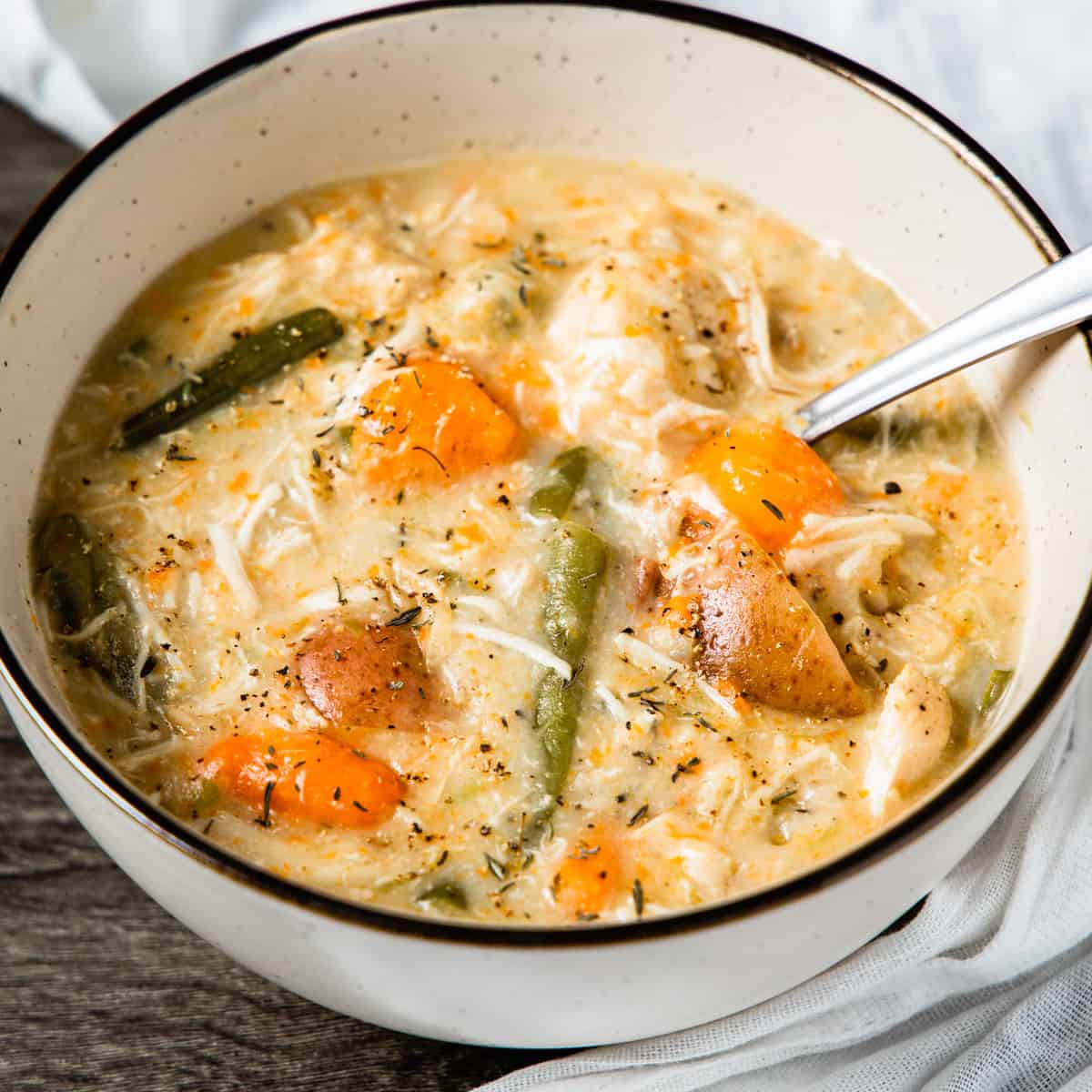 A bowl of creamy chicken stew with carrots, green beans, and potatoes.