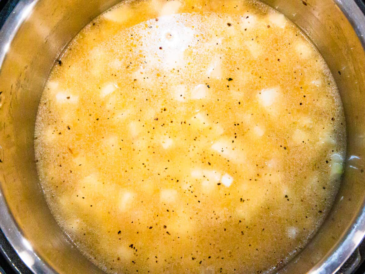 Instant Pot shown filled with chicken broth, diced potatoes, and onions before pressure cooking.