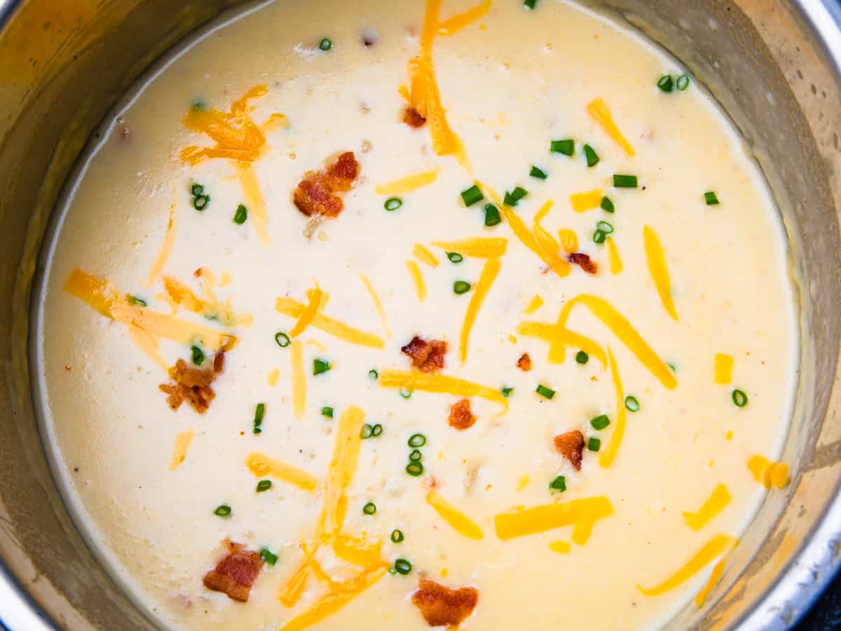 Potato soup shown in an Instant Pot topped with cheese, bacon, and chives.