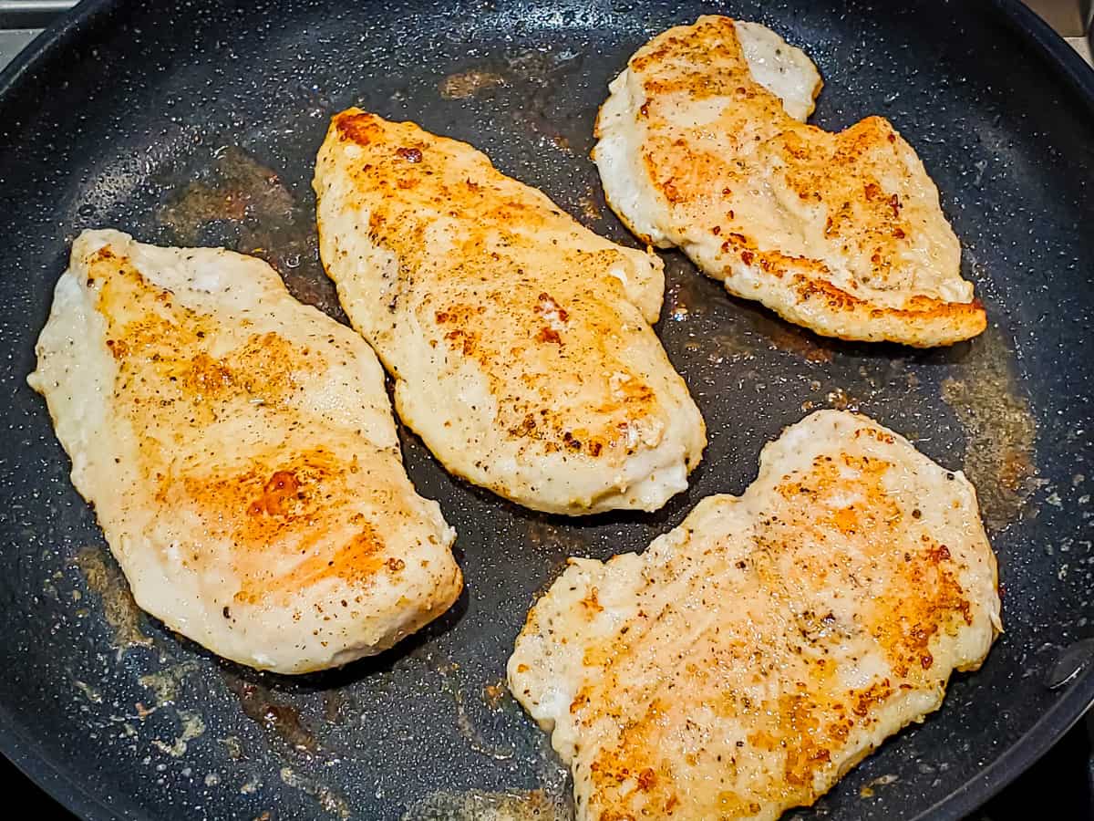 Chicken breasts being cooked in a skillet until golden brown.