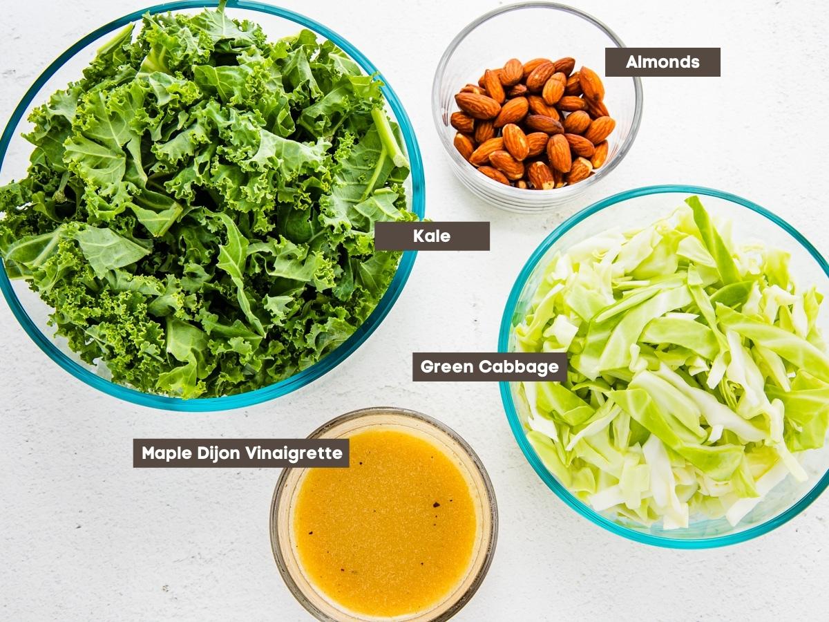 The kale salad ingredients and prepared vinaigrette dressing are shown arranged on a countertop.