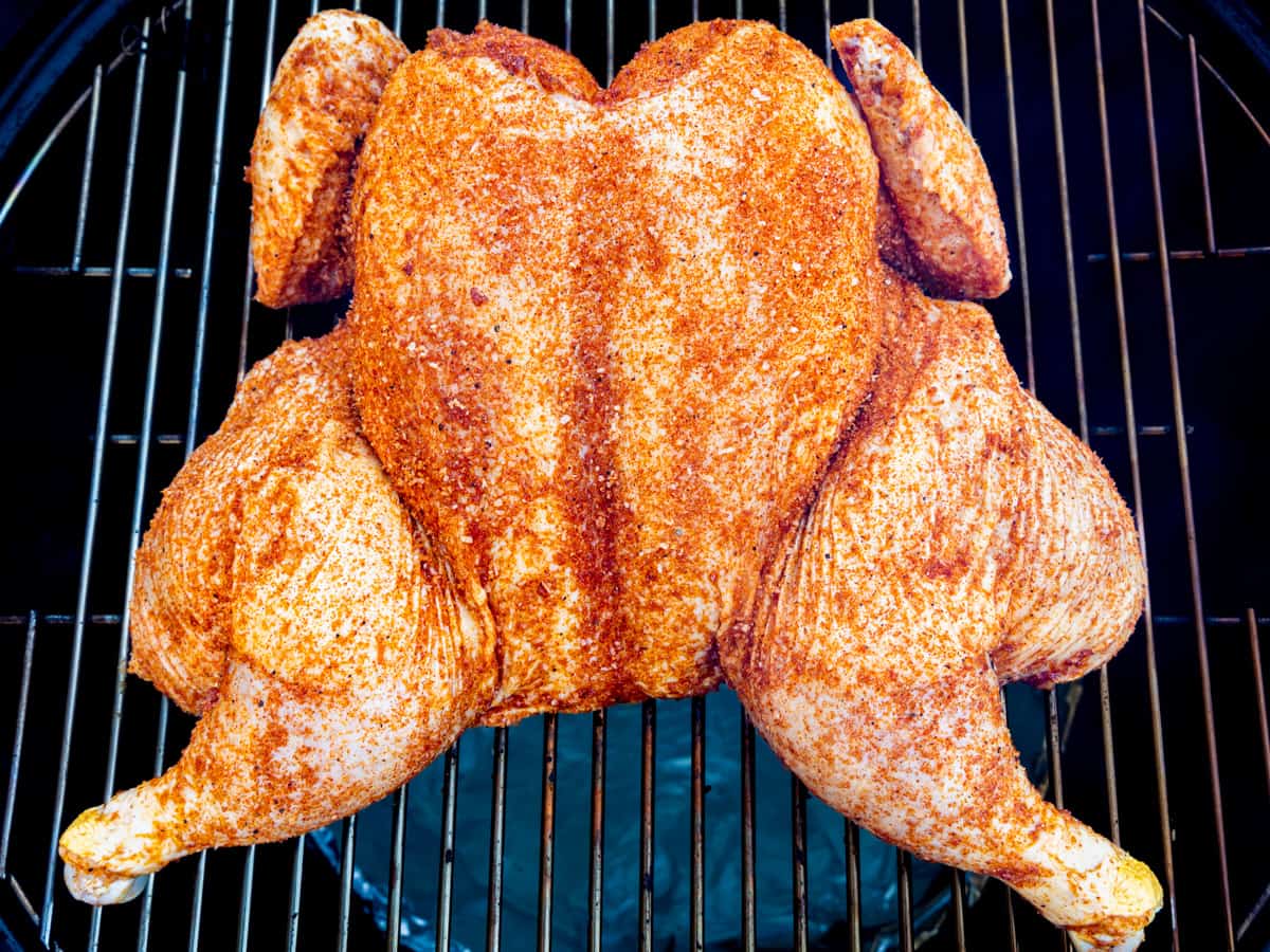 A whole chicken shown on a smoker before being cooked.