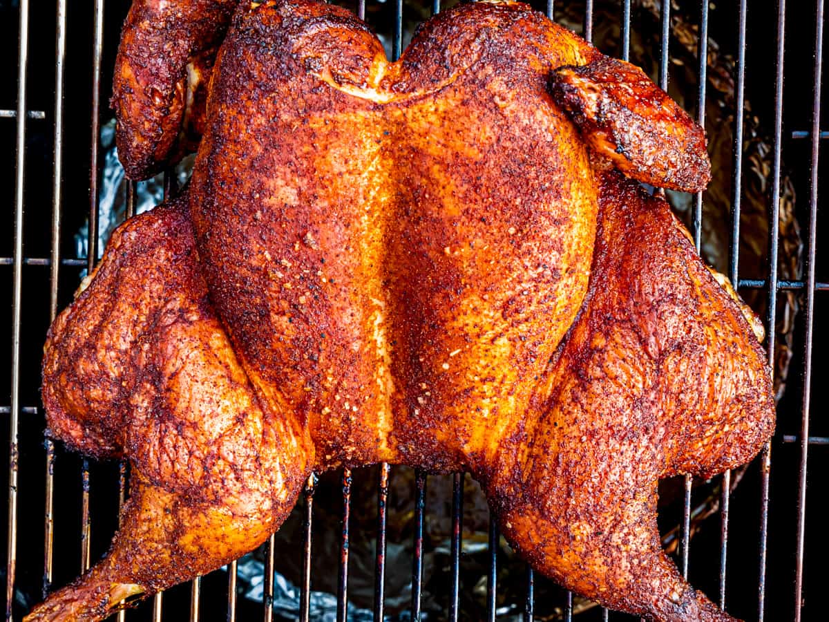 A whole chicken shown on a smoker after being cooked.