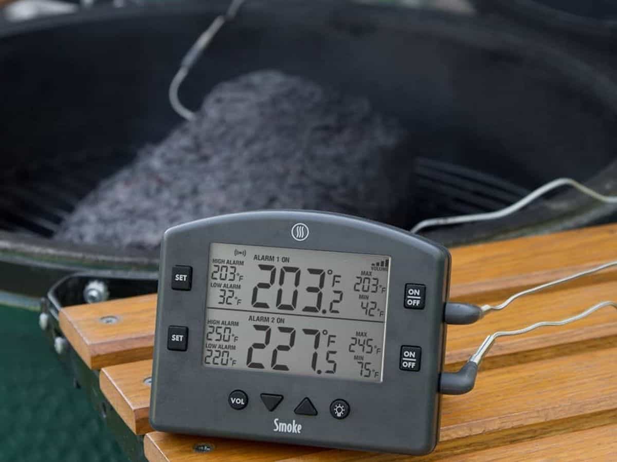 A digital thermometer with multiple temperature probes, shown next to a grill. 