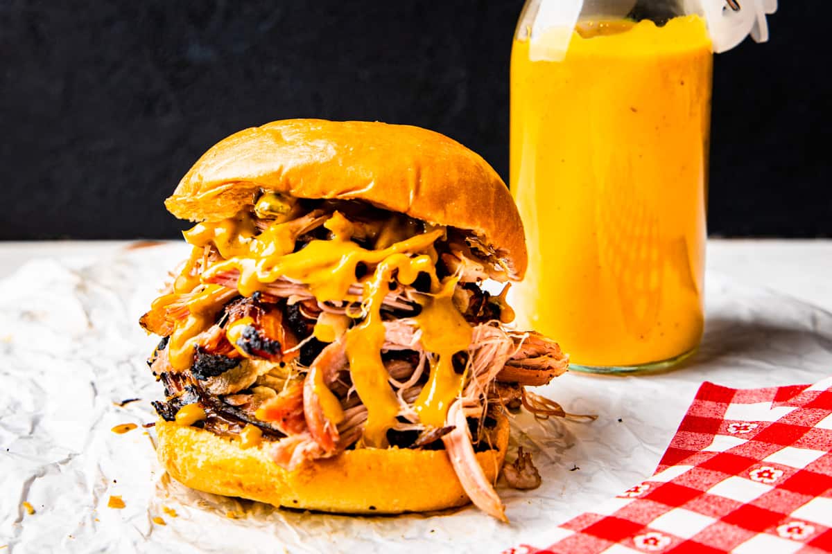 Close up of a pulled pork sandwich dripping with Carolina gold BBQ sauce.