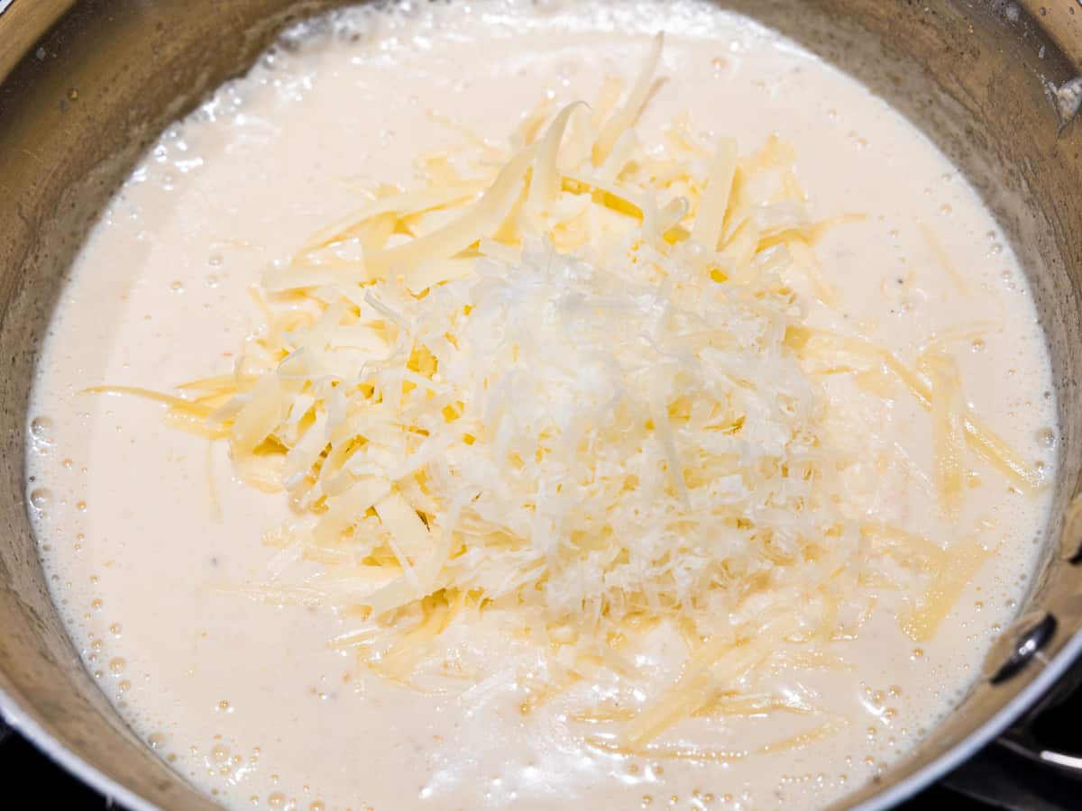 Bechamel sauce for cauliflower gratin shown in a saucepan with shredded cheese on top.