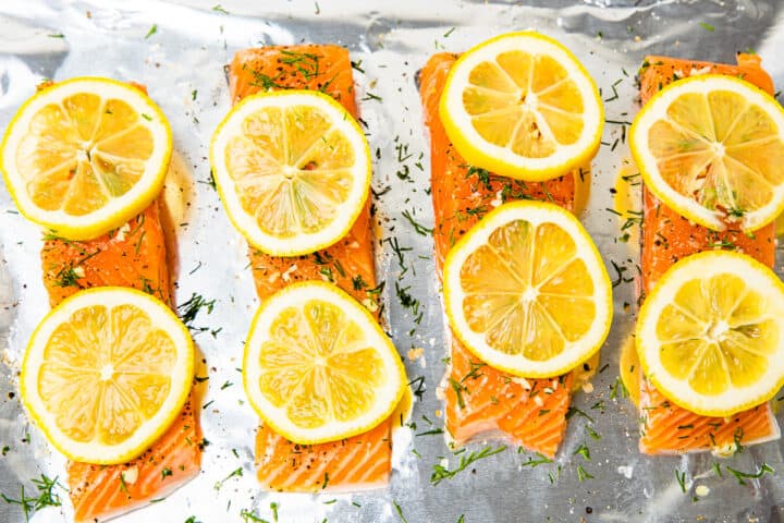 Salmon on a foil lined sheet pan with lemon slices on top.