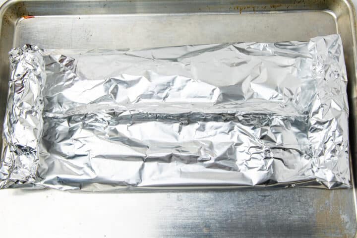 A aluminum foil pouch filled with salmon shown on a sheet pan.