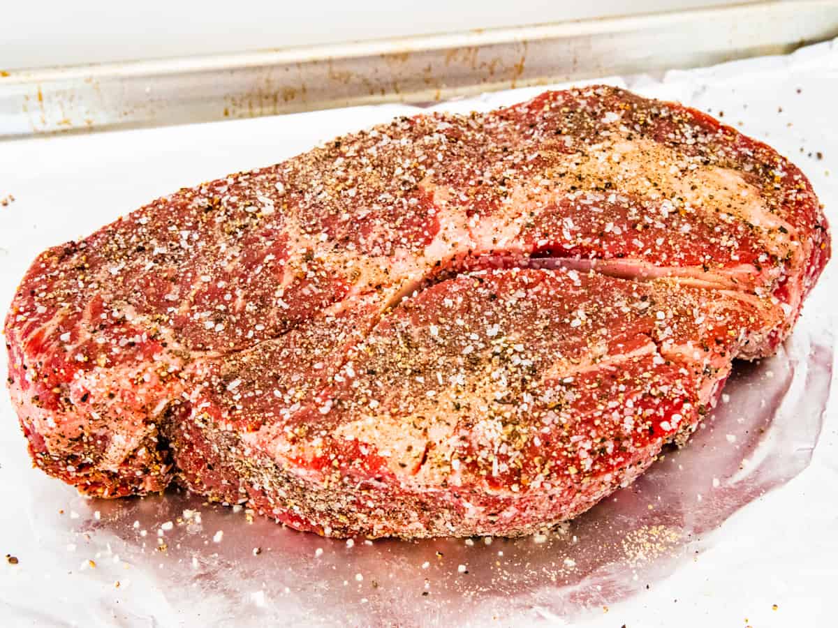 A chuck roast shown after being seasoned with salt, pepper, and garlic powder.