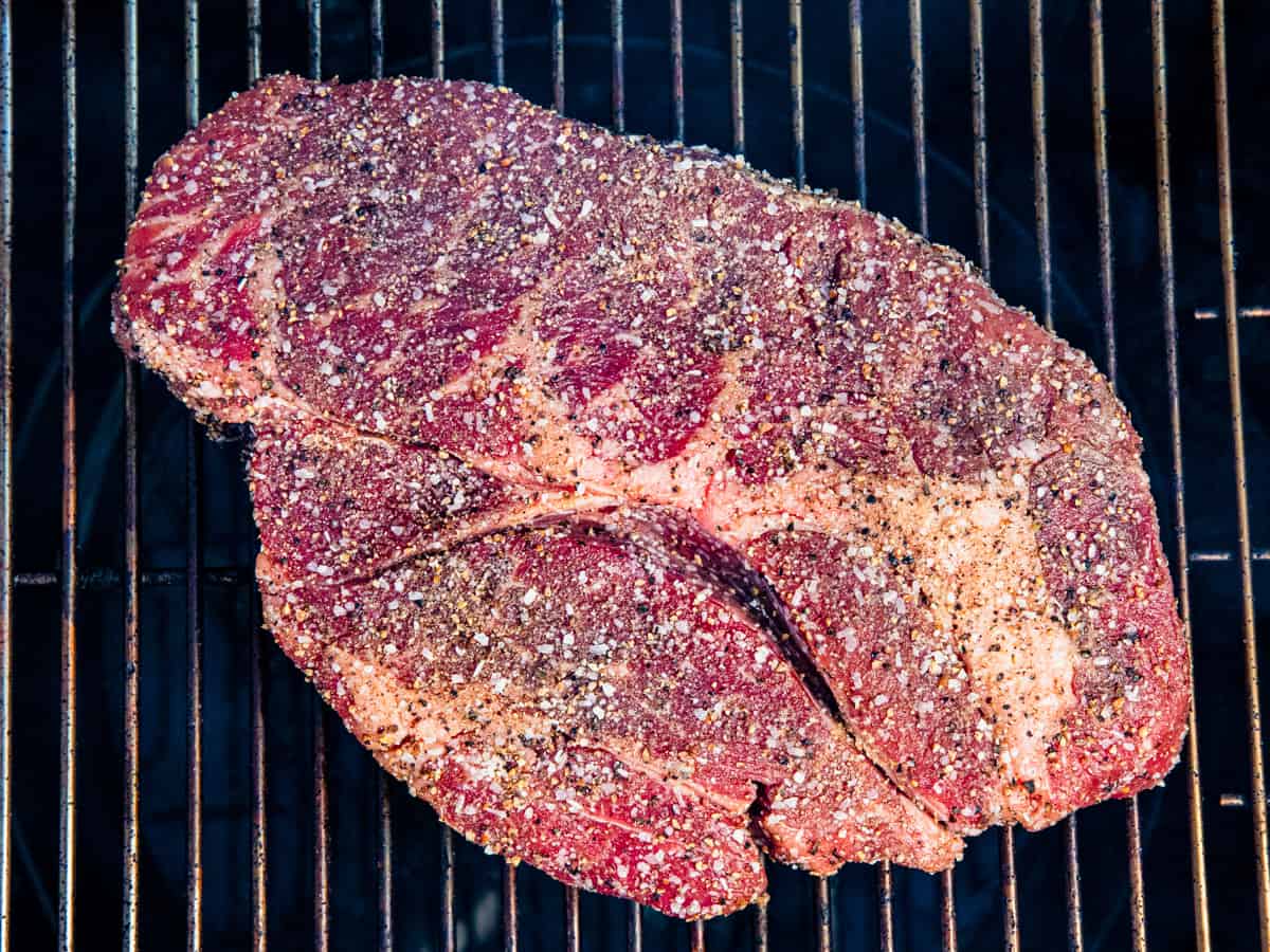 A seasoned chuck roast shown cooking on a smoker.