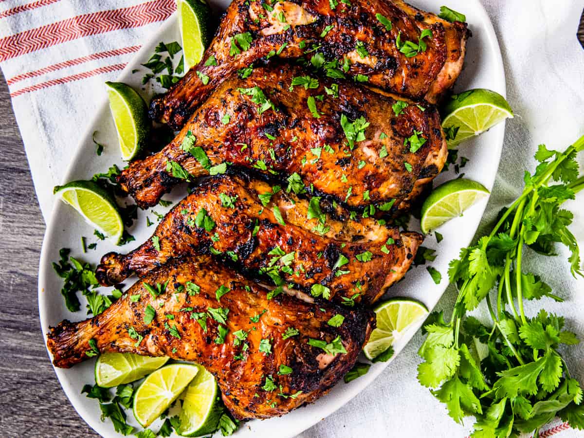 A platter of grilled chicken leg quarters garnished with cilantro and lime. 
