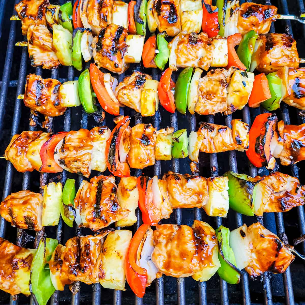 Chicken kebabs coated in huli huli sauce being cooked on a grill. 
