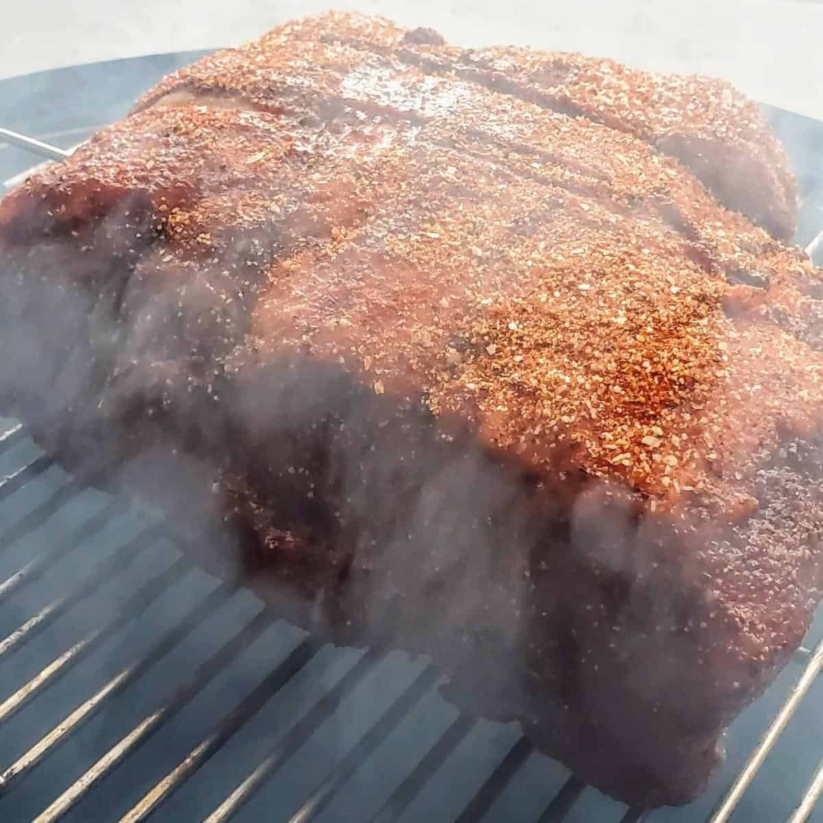 Pork butt cooking on a smoker surrounded by thick smoke.