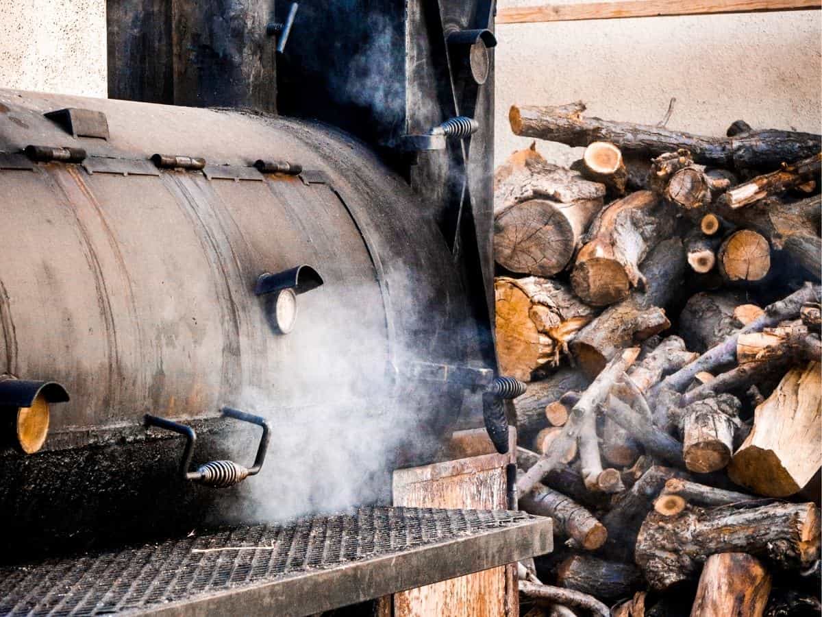Offset smoker shown with a stack of wood.