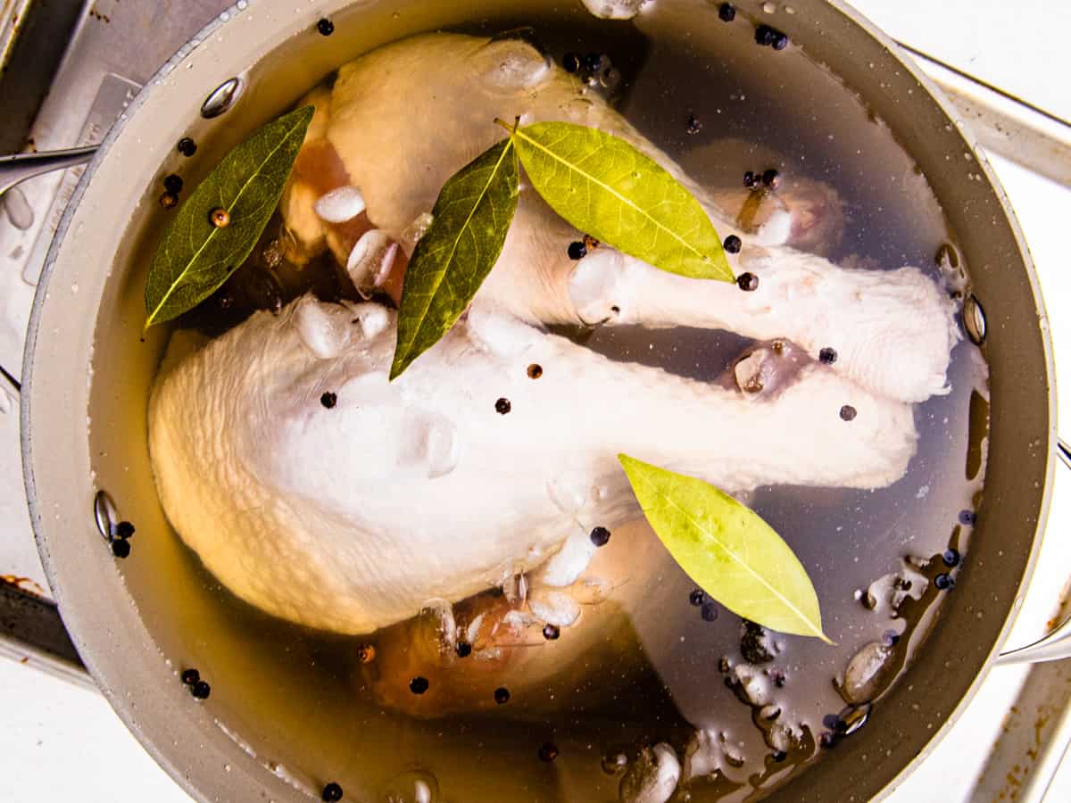 Turkey legs shown submerged in a large stock pot filled with brine.