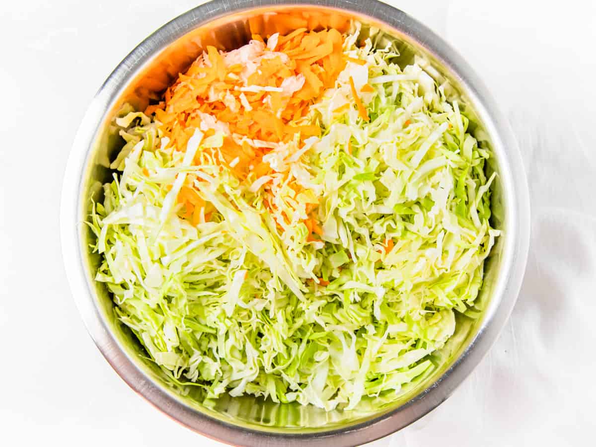 Shredded cabbage, carrot, and onion in a large stainless steel mixing bowl.