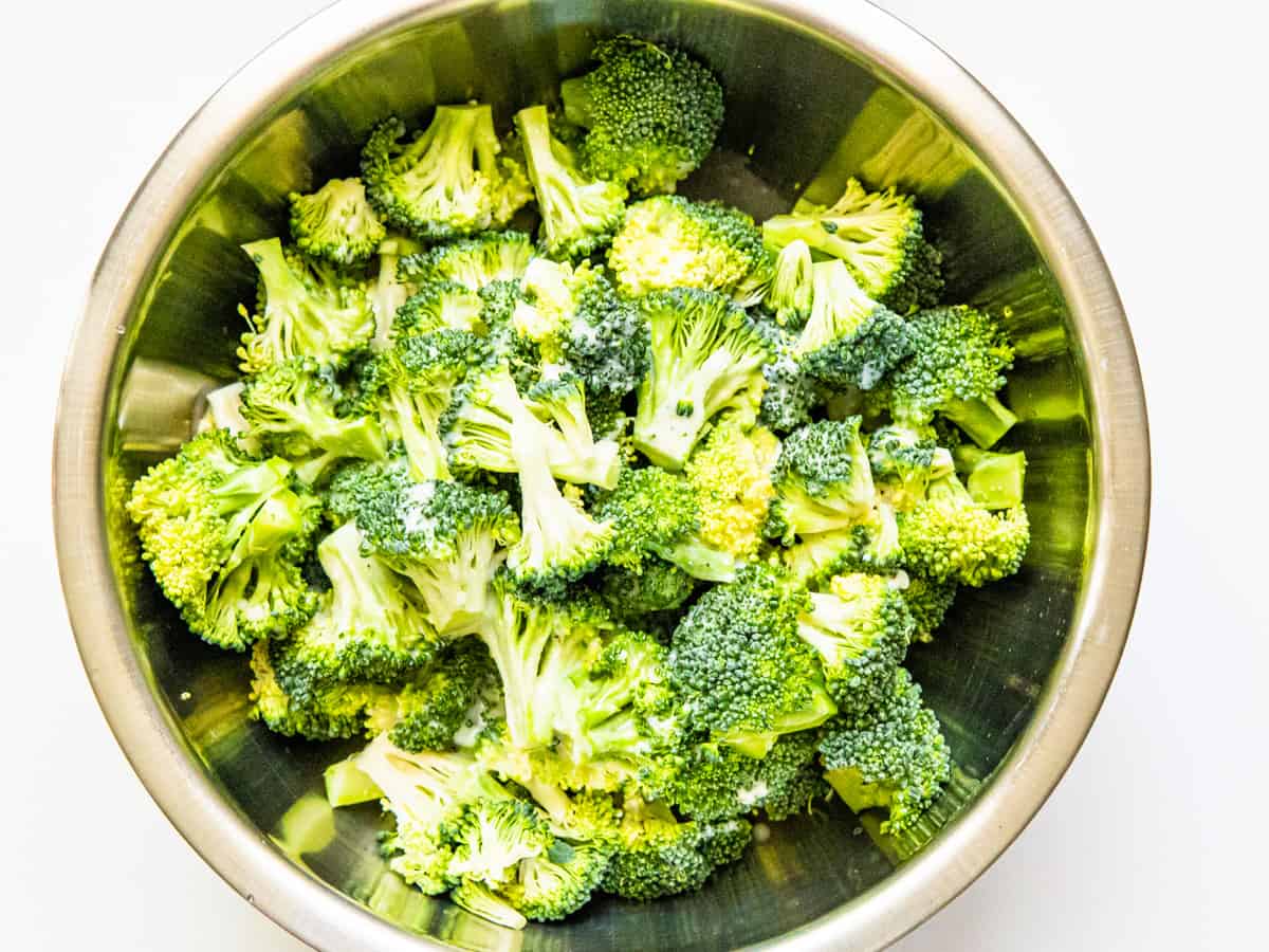 Broccoli florets in a mixing bowl coated with dressing. 