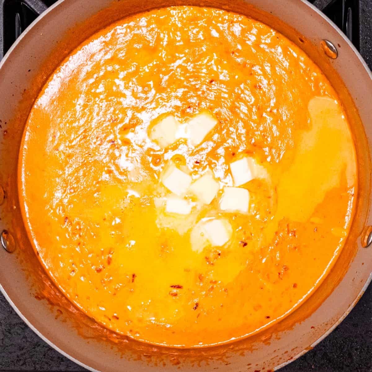 Vodka sauce shown cooking with butter and pasta water added on top. 