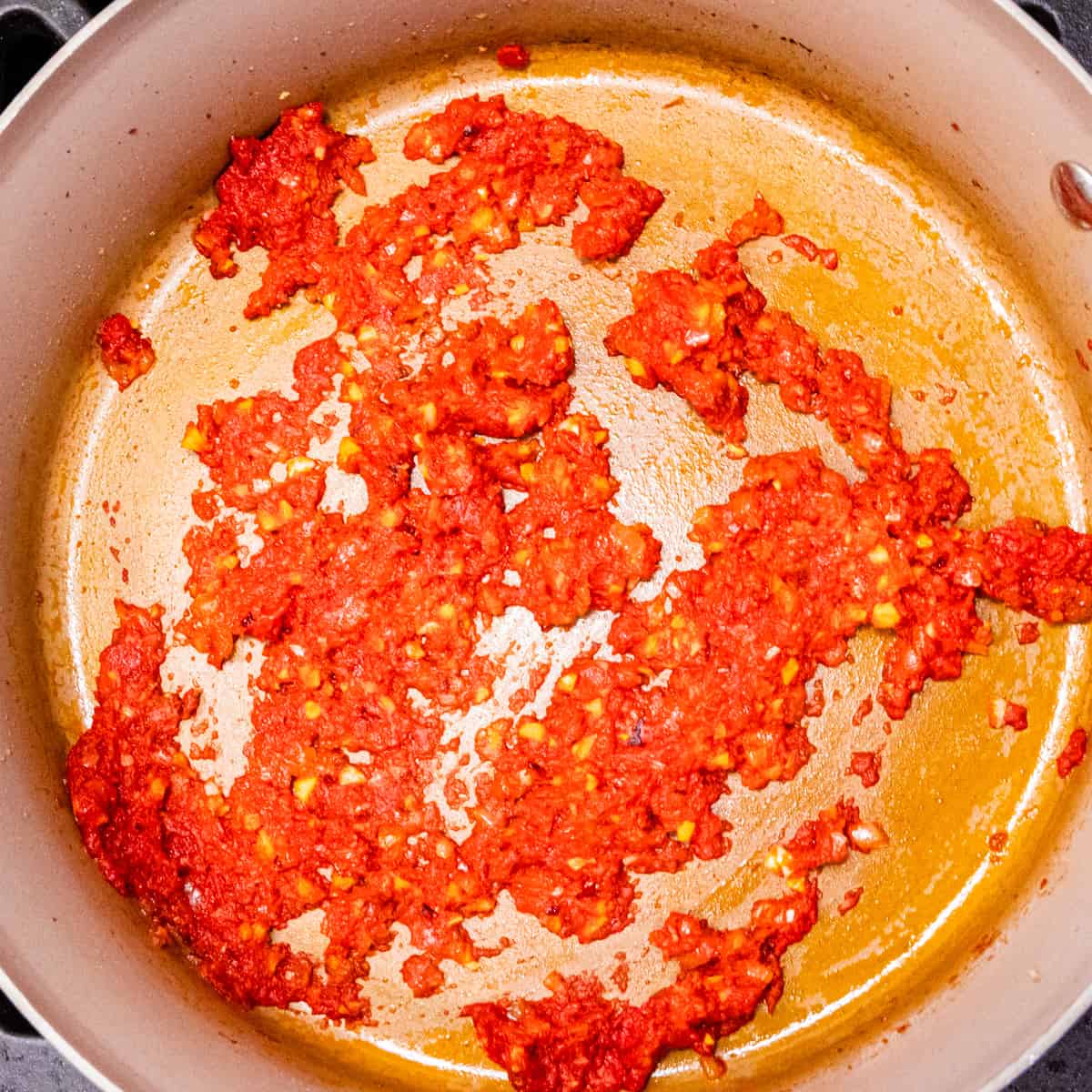 Tomato paste cooking in a saucepan with sautéed shallot and garlic. 