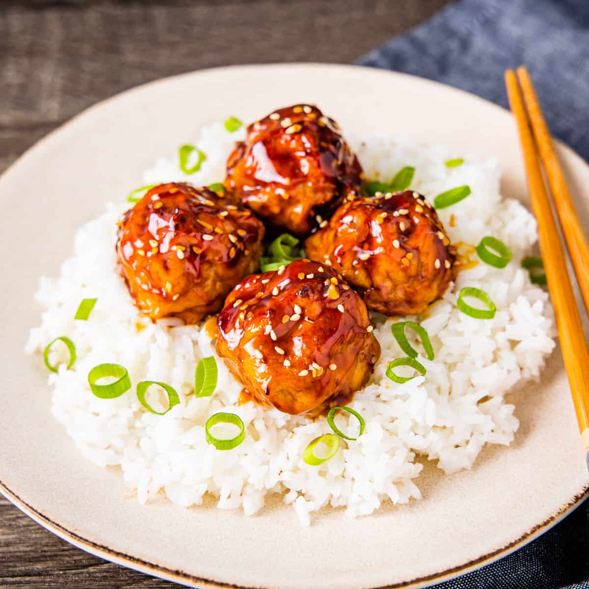 A plate of chicken meatballs with an Asian glaze served on a bed of rice. 