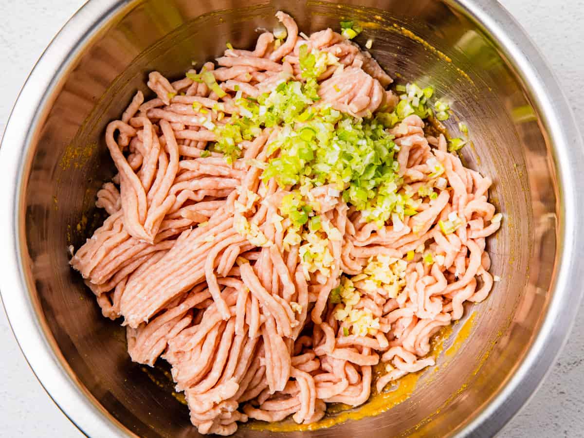 Ground turkey, chopped green onion, and minced garlic are added to the mixing bowl with the breadcrumb mixture. 