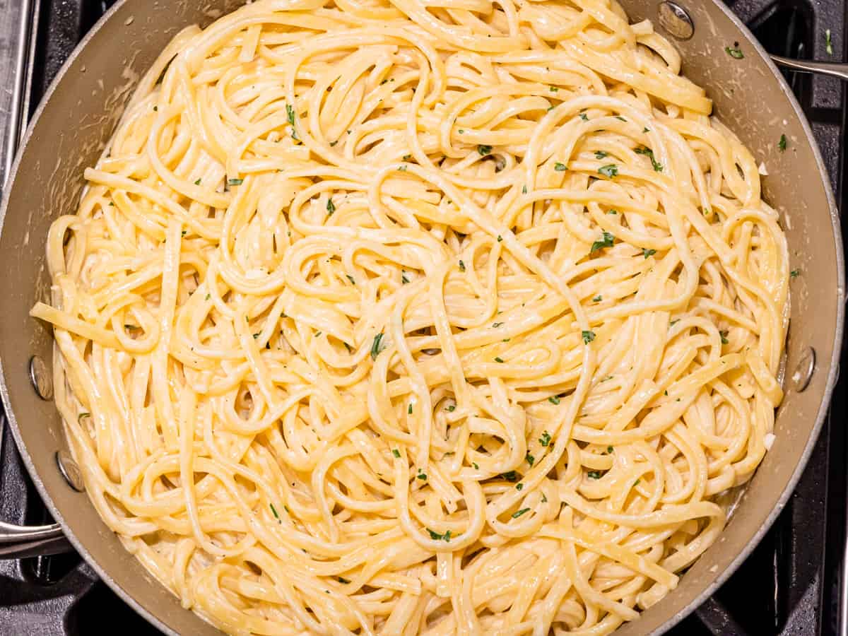 Pasta added to the cream sauce in a large saucepan. 