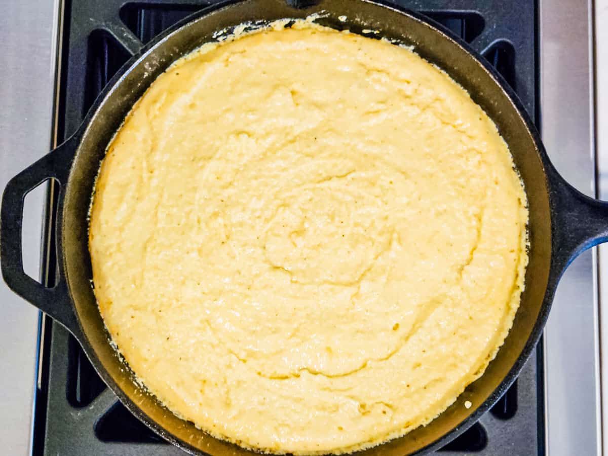 A cast iron skillet filled with uncooked cornbread batter. 