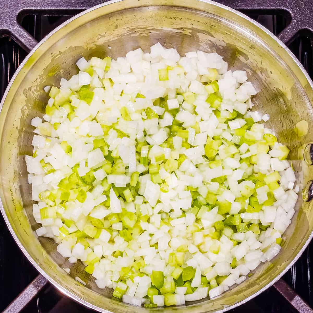 Onions and celery being cooked in a saucepan.