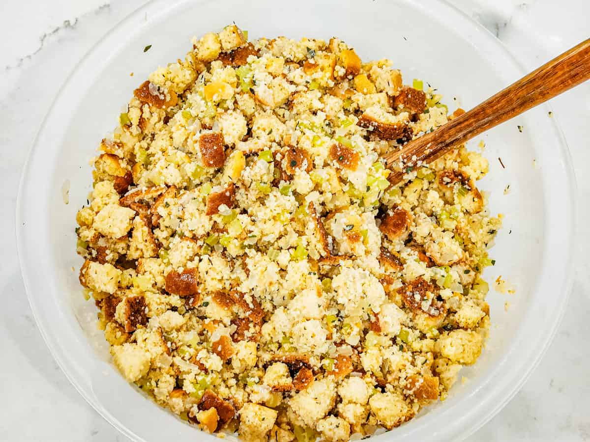 Bread cubes in a large mixing bowl being mixed with the chicken stock and vegetable mixture. 