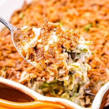 A large scoop of green bean casserole held in front of a large baking dish filled with the casserole.