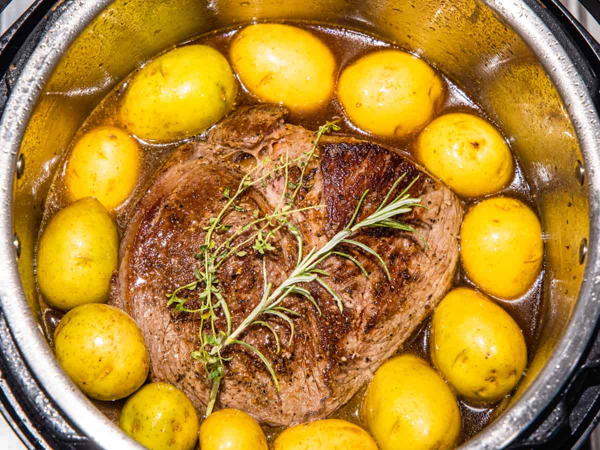 Seared beef pot roast shown in an Instant Pot surrounded by potatoes before being pressure cooked.