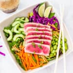 A large bowl of chopped salad topped with sliced seared tuna and served with an Asian soy vinaigrette dressing.