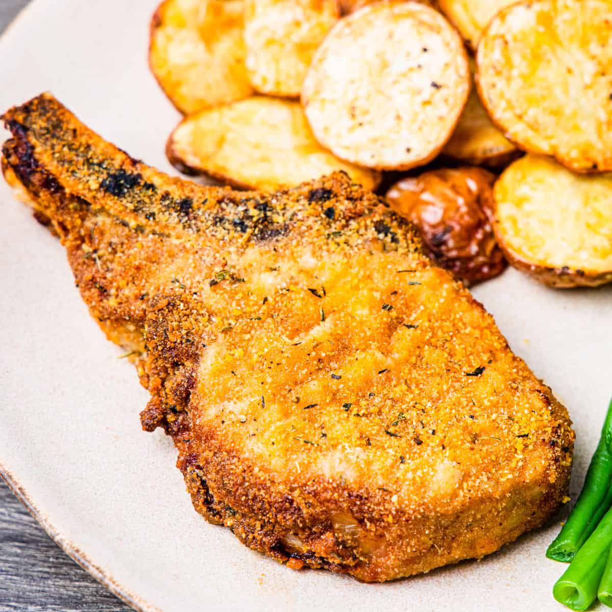 Close up of an oven fried pork chop served on a plate with roasted potatoes. 