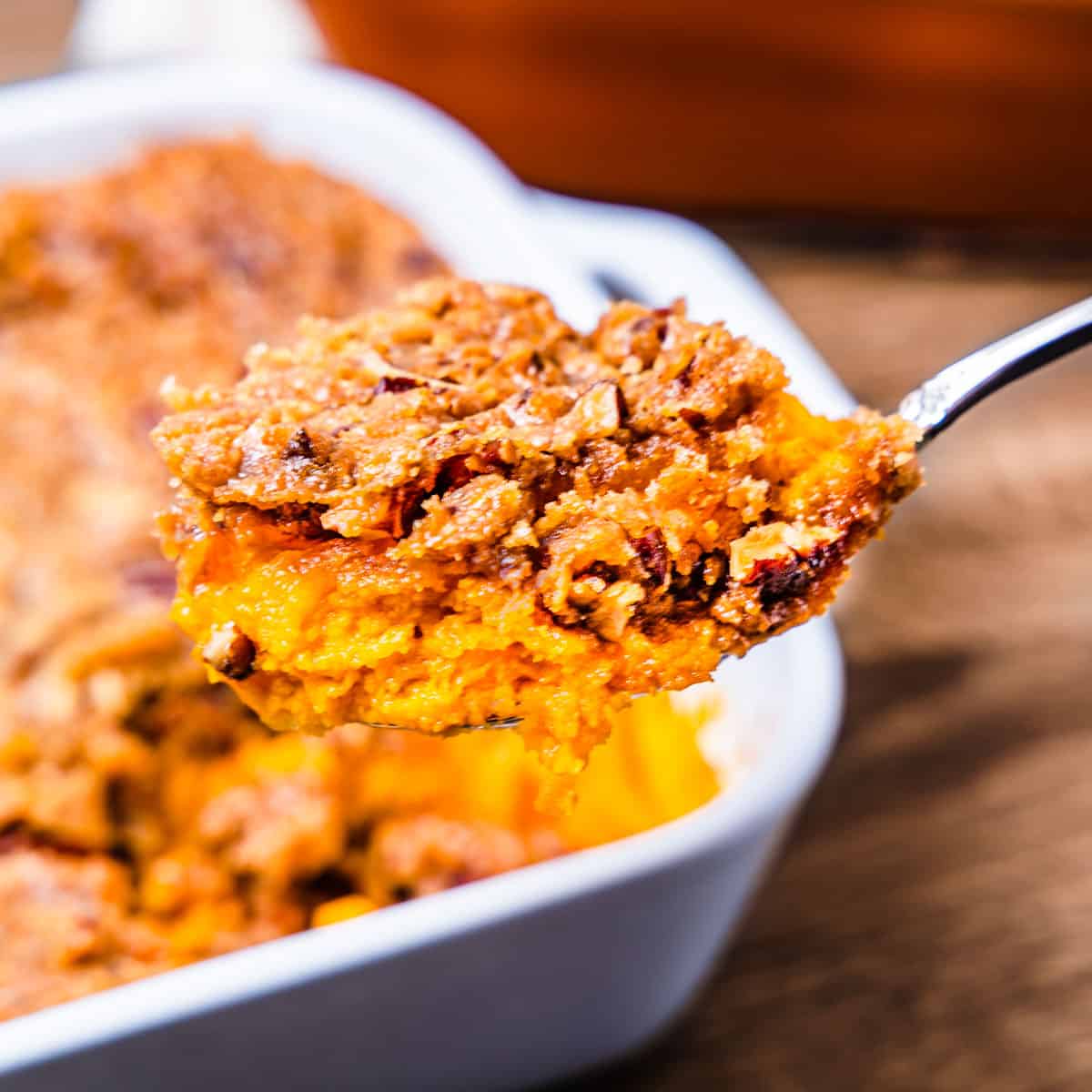 A large scoop of sweet potato souffle on a serving spoon held in front of the casserole dish. 
