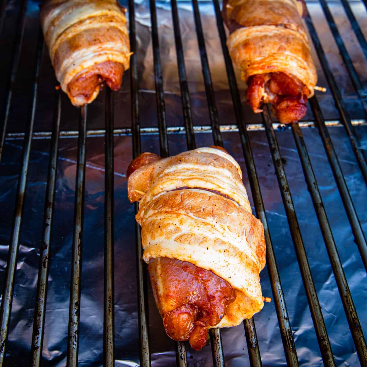 Chicken thighs wrapped in bacon on a smoker before cooking.