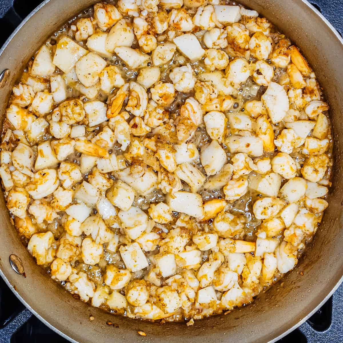 Shrimp and scallops cooking in a pan with shallots and garlic.