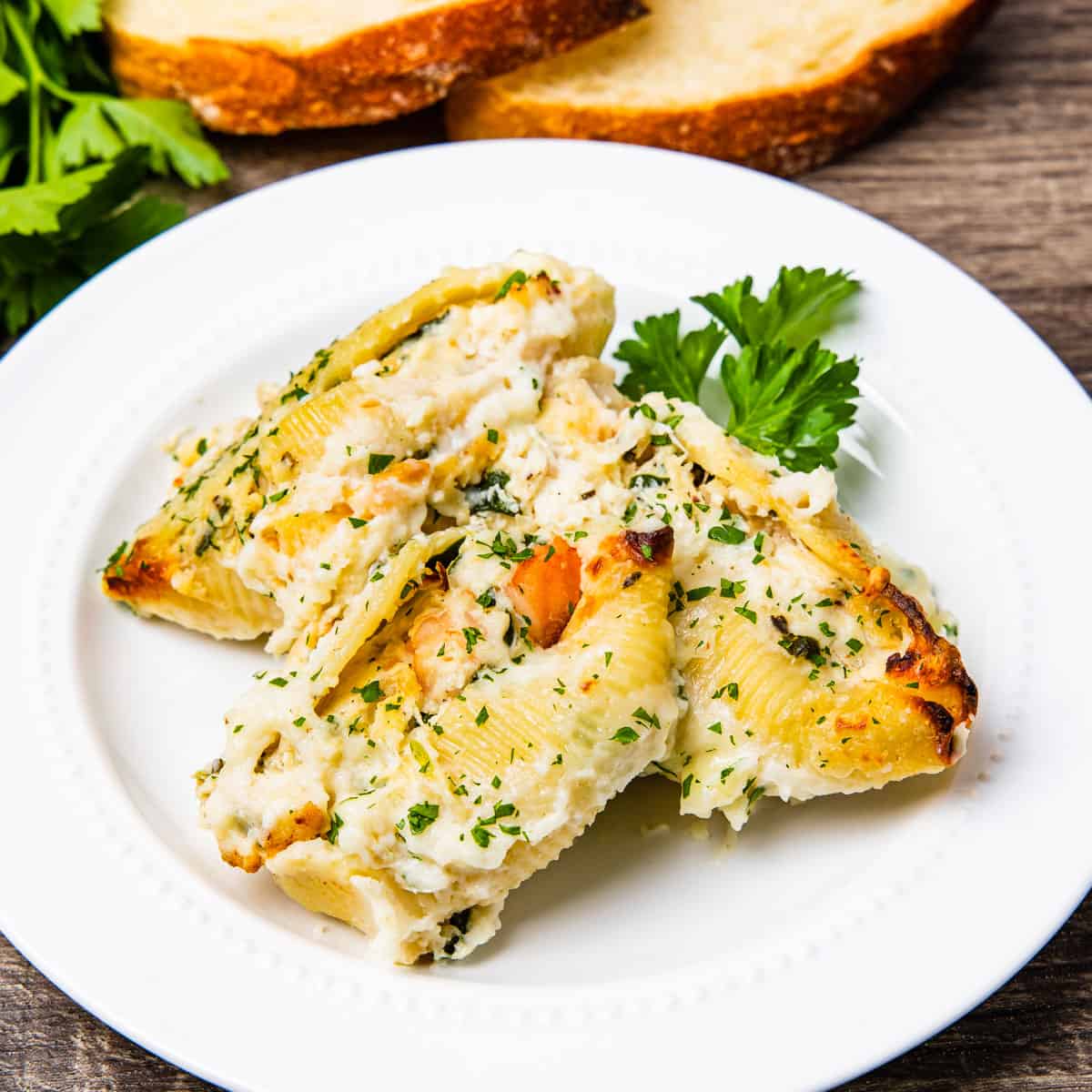 A serving of baked pasta shells stuffed with a seafood and ricotta filling covered in a creamy sauce.