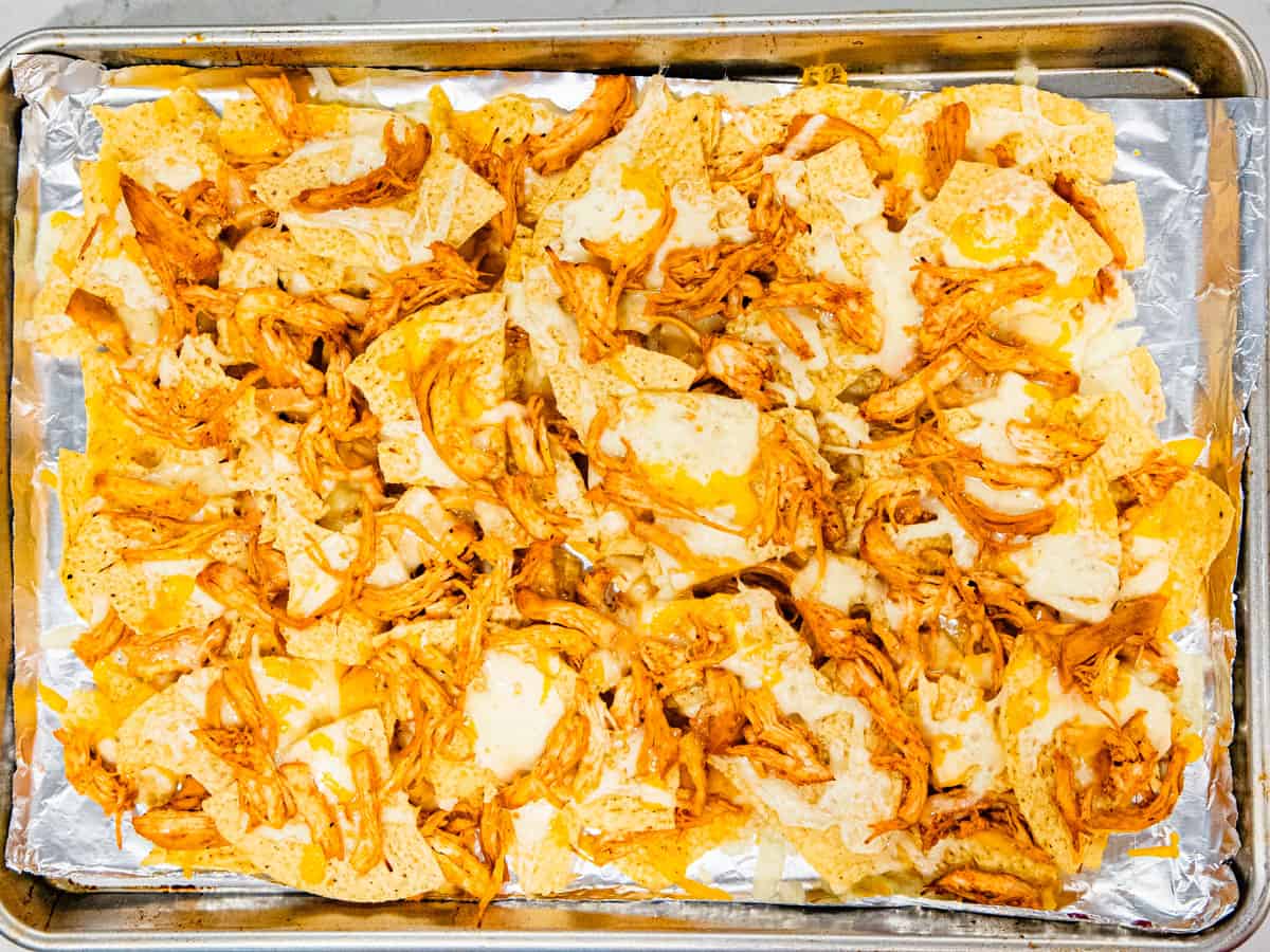 BBQ chicken nachos shown on a sheet pan after being baked, but prior to adding additional toppings.