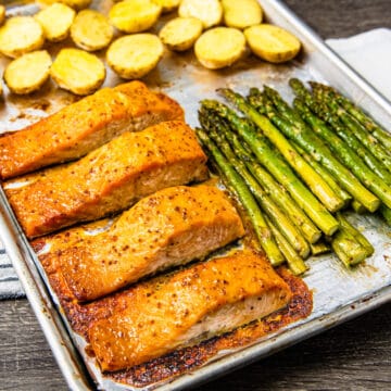 Salmon filets coated with a honey mustard glaze on a sheet pan with asparagus and potatoes.