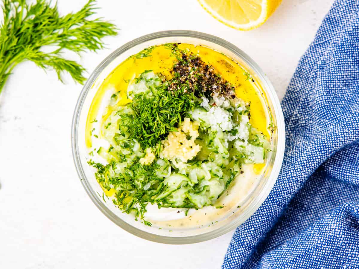 Ingredients for tzatziki sauce shown in a mixing bowl before stirring together.