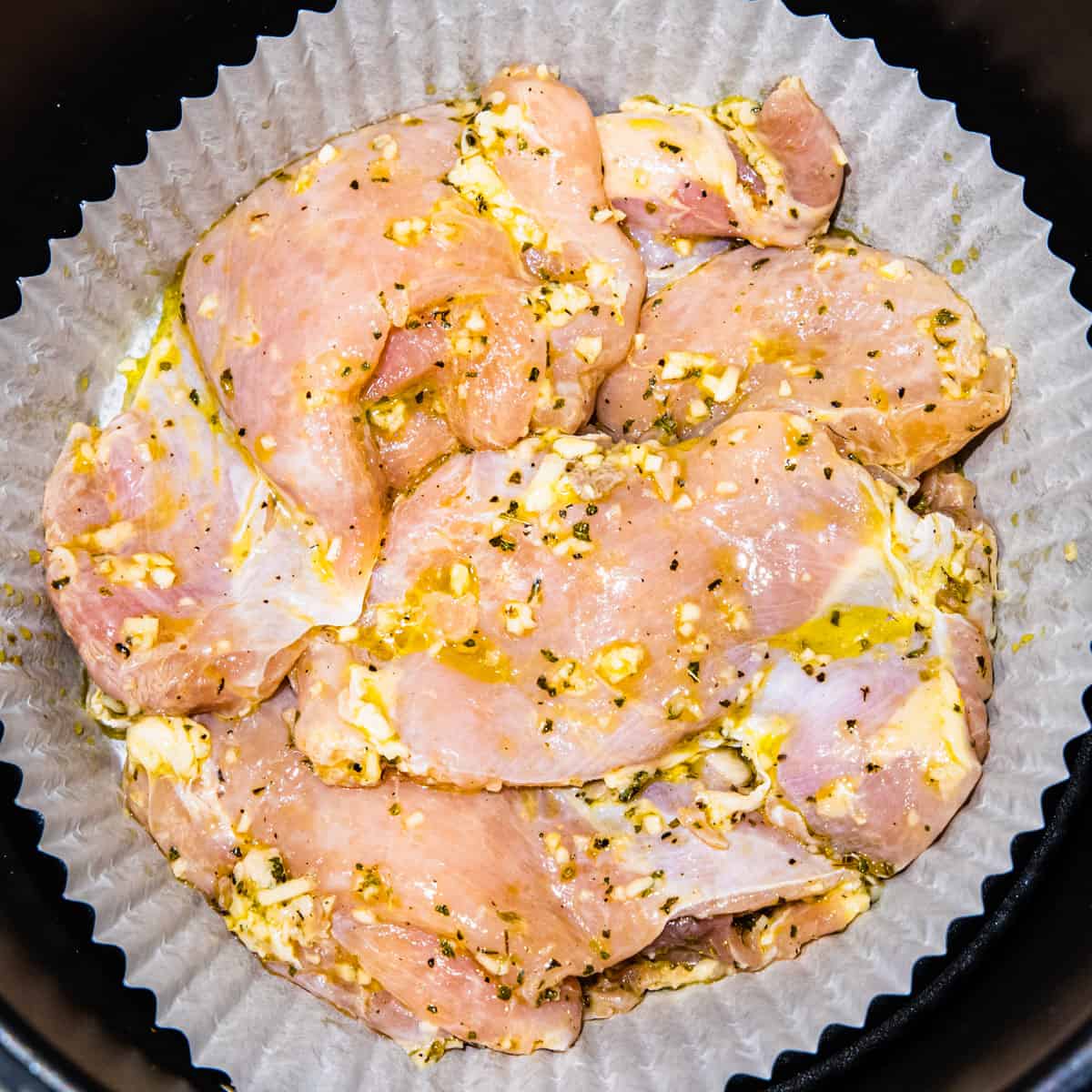 Skinless chicken thighs in an air fryer basket before being cooked.