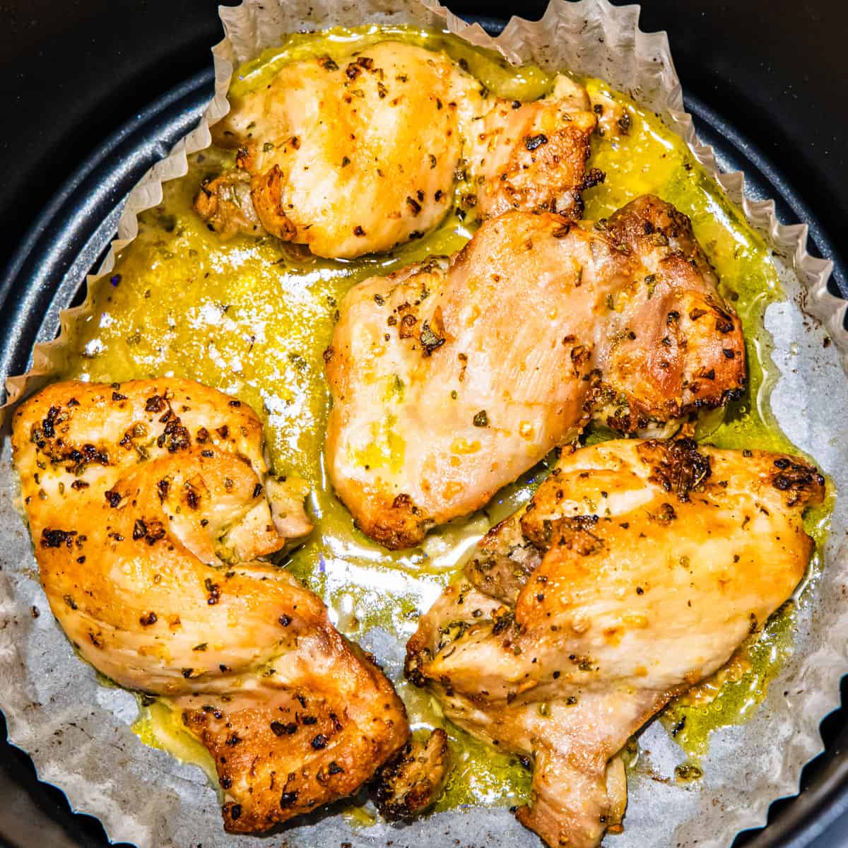 Cooked chicken thighs in an air fryer basket.