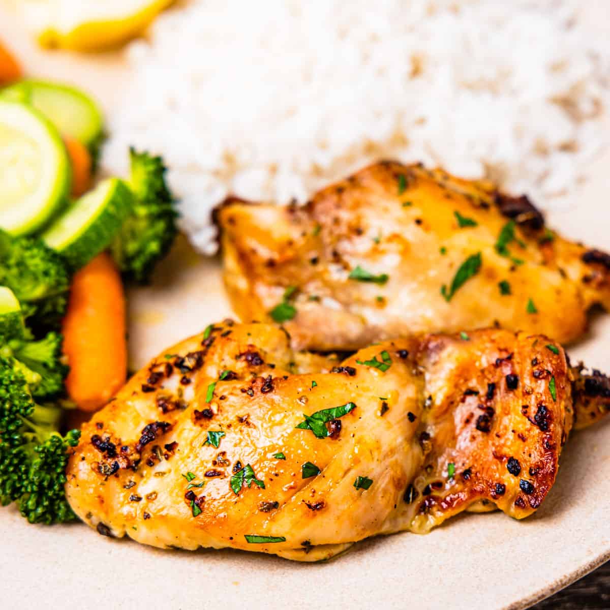Close-up of two boneless skinless chicken thighs served on a plate with steamed vegetables and rice.