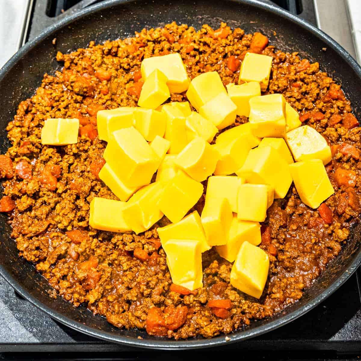 Cubes of Velveeta cheese on top of chili, cooking in a large sskillet. 