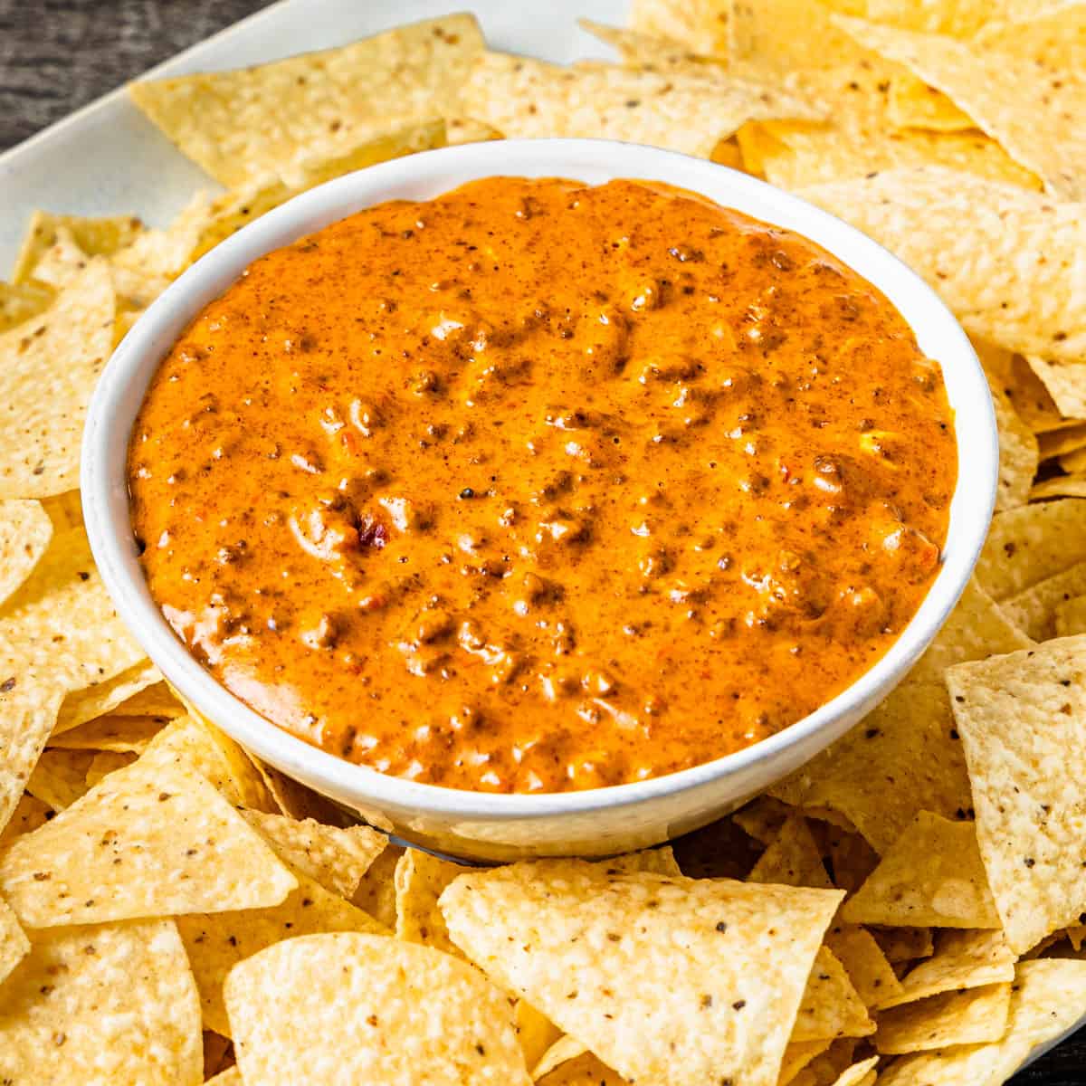 A bowl of chili cheese dip surrounded by tortilla chips.