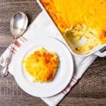 A cheesy hashbrown casserole on a table with a serving on a small plate next to the casserole dish.